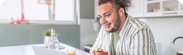 Jeune homme tenant son café devant son laptop